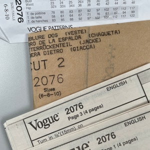 May include: A close-up of a Vogue sewing pattern for sizes 6-8-10. The pattern is for a jacket and includes instructions for cutting and sewing. The pattern number is 2076.