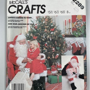 May include: A vintage sewing pattern for making Santa Claus and a child's Christmas costume. The pattern is from McCall's Crafts and includes instructions for making a Santa doll, a bag, and a child's costume. The pattern is for sizes small and petite.