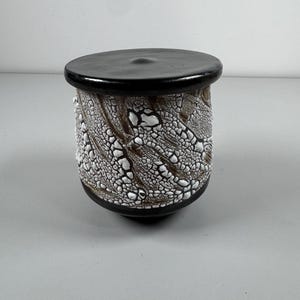 May include: A ceramic jar with a black lid and a white and brown crackle glaze pattern.