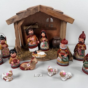 May include: A handcrafted nativity scene with a wooden stable, figurines of Mary, Joseph, baby Jesus, angels, and the three wise men. The figurines are painted with colorful details and patterns. A lamb and donkey are also included.