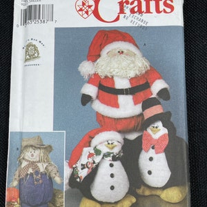 May include: A Simplicity Crafts sewing pattern for making a Santa Claus, a snowman, and a penguin. The pattern is for sizes one to three. The pattern is on a white background with a red heart and the words "Simplicity Crafts" in black.