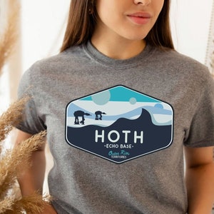 May include: Sport grey t-shirt featuring a graphic of the Hoth Echo Base from a science fiction film. The design includes AT-AT walkers, a mountain range, and the text "HOTH - Echo Base".