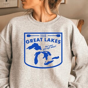 May include: A light gray sweatshirt with a blue graphic that reads "THE GREAT LAKES" with a map of the Great Lakes. The text "Not your average lakes!" is below the main text. The sweatshirt is a crew neck style.