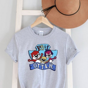May include: Gray t-shirt with a cartoon graphic of three otters with the text "PB&J Otter" on a blue background.