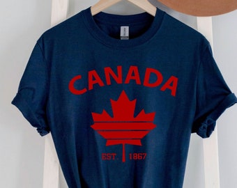May include: Navy blue t-shirt with a red maple leaf graphic and the text "CANADA EST. 1867".