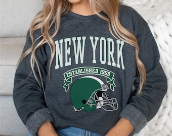 May include: A dark gray sweatshirt with a white graphic print that says "NEW YORK ESTABLISHED 1959" with a green football helmet.