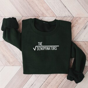 May include: A dark green sweatshirt with the text "THE √DENOMINATORS" printed in white on the front.