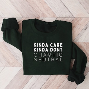 Puede incluir: Una sudadera verde oscuro con texto blanco que dice "Kinda Care Kinda Don't Chaotic Neutral" y un gráfico de dado de 20 caras blanco.