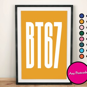 May include: A framed print with a yellow background and white text that reads "BT67". The text is in a bold, sans-serif font. The frame is black and the print is surrounded by a white border. The text "Any Postcode" is printed in white on a pink circle in the lower right corner of the print.
