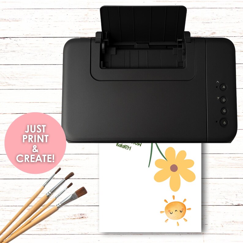 May include: A black printer with the top open, printing a white sheet with a yellow flower and smiling sun illustration. The text "JUST PRINT & CREATE!" is in a pink circle. Paintbrushes are in the lower left.