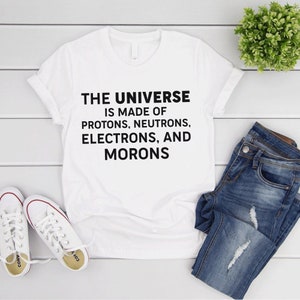May include: White t-shirt with black text that reads "THE UNIVERSE IS MADE OF PROTONS, NEUTRONS, ELECTRONS, AND MORONS".