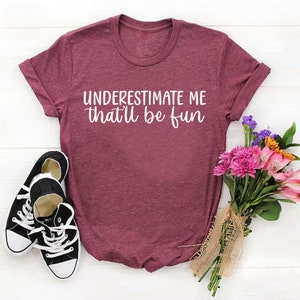 May include: A maroon t-shirt with the text "UNDERESTIMATE ME that'll be fun" in white lettering.