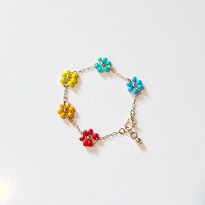 Pode incluir: Um bracelete de contas coloridas com pingentes em forma de flor em tons de amarelo, azul e vermelho.