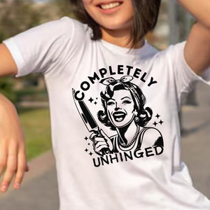 May include: White t-shirt with a black and white illustration of a woman holding a knife and the text "COMPLETELY UNHINGED".