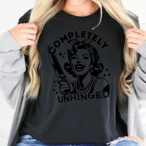 May include: Black t-shirt with a graphic of a woman holding a knife and the text "COMPLETELY UNHINGED".