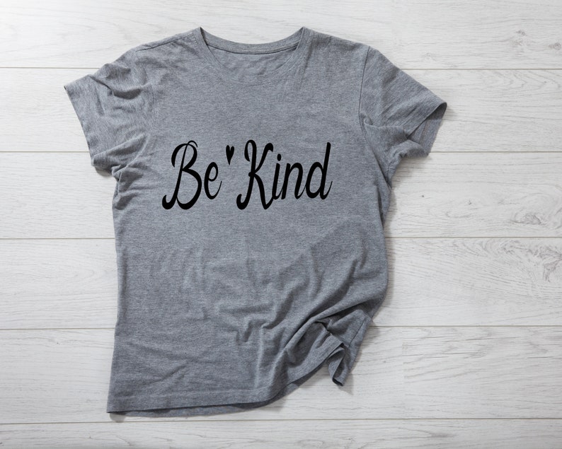 K&ouml;nnte beinhalten: Graues T-Shirt mit dem Text "Be' Kind" in schwarzer Kursivschrift.