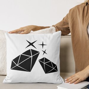 May include: White cushion with a black diamond design and sparkling stars. The cushion is on a white sofa.