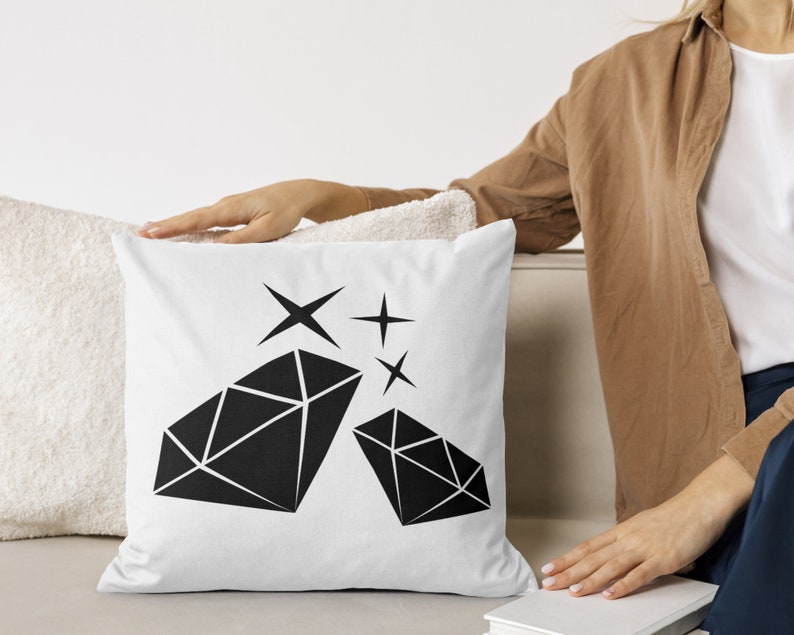 May include: White cushion with a black diamond design and sparkling stars. The cushion is on a white sofa.