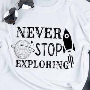 Puede incluir: Camiseta blanca con texto negro que dice "NEVER STOP EXPLORING" con un cohete y un planeta.