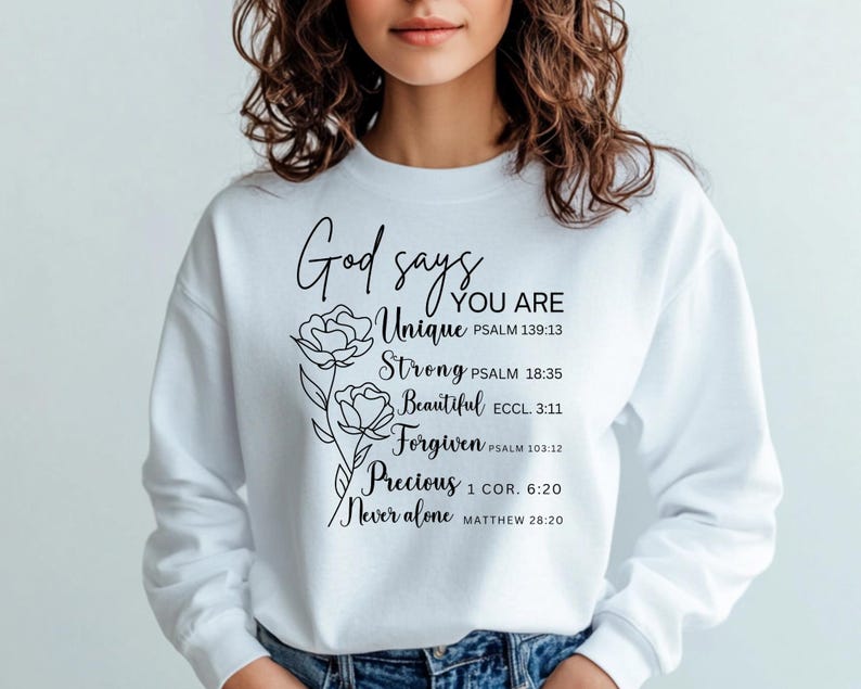 May include: White sweatshirt with black text that reads "God says you are Unique, Strong, Beautiful, Forgiven, Precious, Never alone" with bible verses listed below each word. The text is surrounded by a floral design.