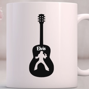 May include: White ceramic mug with a black silhouette of a guitar with the name "Elvis" written on it. The silhouette of Elvis Presley is inside the guitar.