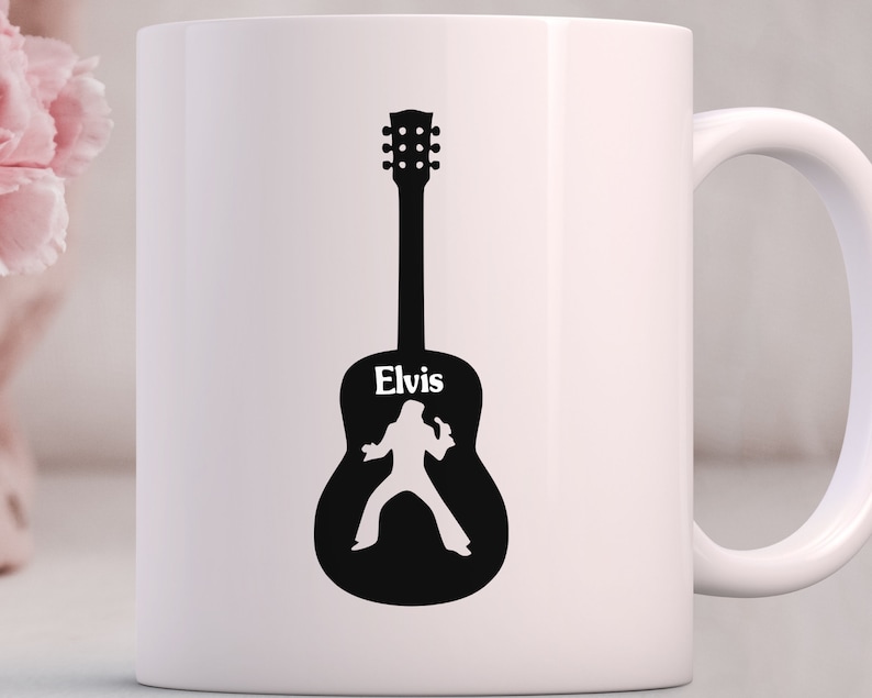 May include: White ceramic mug with a black silhouette of a guitar with the name "Elvis" written on it. The silhouette of Elvis Presley is inside the guitar.