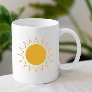 May include: White ceramic mug with a yellow sun graphic. The sun has a yellow center and white rays.
