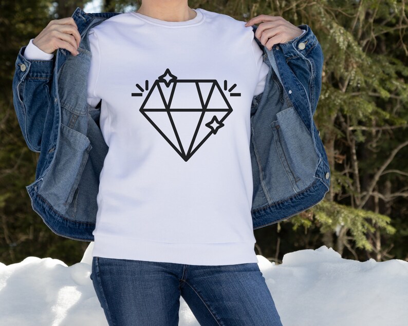 May include: A white sweatshirt featuring a black diamond graphic and two small stars. The sweatshirt is being held by a person wearing a denim jacket and blue jeans.