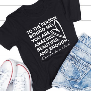K&ouml;nnte beinhalten: Schwarzes T-Shirt mit wei&szlig;em Text, der lautet: "To the person behind me: You are amazing, beautiful and enough. Remember that."