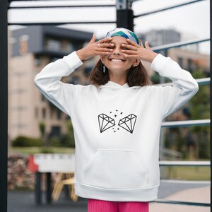May include: White hoodie with a black diamond graphic and small stars. The hoodie has a drawstring hood and a kangaroo pocket.
