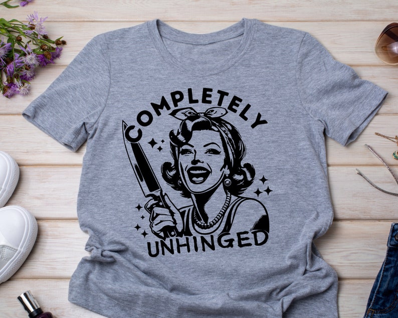 May include: Gray t-shirt with a black graphic of a woman holding a knife and the text "COMPLETELY UNHINGED".