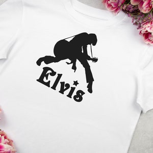 May include: White t-shirt with a black silhouette of Elvis Presley playing a guitar and the word "Elvis" printed below.