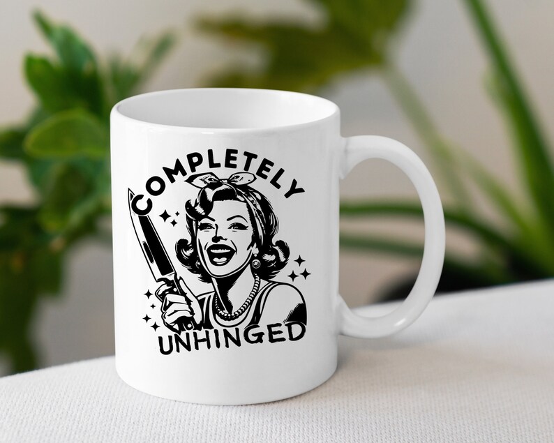 May include: White ceramic mug with a black and white illustration of a woman holding a knife. The text "COMPLETELY UNHINGED" is printed on the mug.