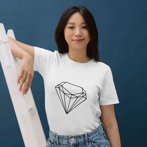 May include: A white t-shirt featuring a black geometric diamond design. The model is wearing the shirt and leaning against a white ladder.
