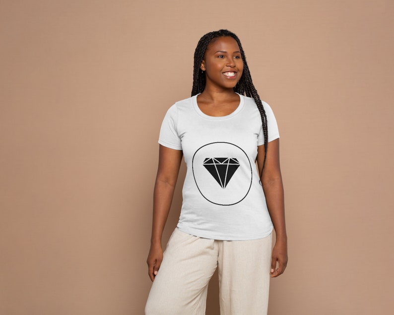 May include: A white t-shirt featuring a black diamond graphic within a circle. The diamond is a geometric shape with multiple points.