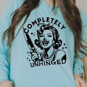 May include: A light blue sweatshirt with a black graphic of a woman holding a knife and the text "COMPLETELY UNHINGED".