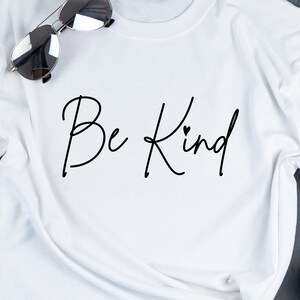 K&ouml;nnte beinhalten: Wei&szlig;es T-Shirt mit dem Text "Be Kind" in schwarzer Kursivschrift mit einem kleinen Herzen &uuml;ber dem "d".