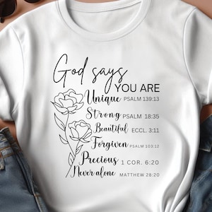 May include: White t-shirt with black text and a floral design. The text reads "God says you are Unique, Strong, Beautiful, Forgiven, Precious, Never alone" with corresponding bible verses.