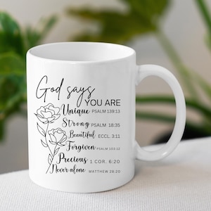 May include: White ceramic coffee mug with a black design that reads "God says you are Unique, Strong, Beautiful, Forgiven, Precious, Never alone" with bible verses listed below each word.