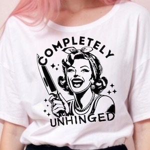 May include: White t-shirt with a black and white illustration of a woman holding a knife. The text "COMPLETELY UNHINGED" is printed on the shirt.
