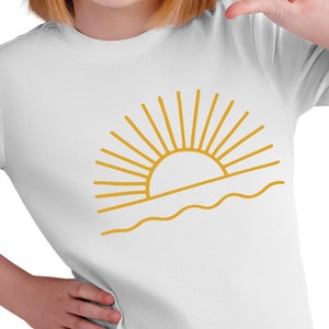 May include: A white t-shirt with a gold outline of a sun setting over the ocean.