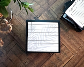 May include: A black and white notepad with a palm leaf design and horizontal lines. The notepad is in a black box, with the text "Live Happy Labs" at the bottom. Other notepads are visible in the background.