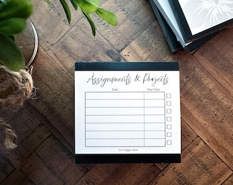May include: A black and white notepad with the words "Assignments & Projects" at the top. The notepad has lines for tasks and due dates, with check boxes. The words "Live Happy Label" are at the bottom.