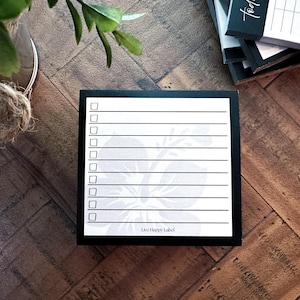 May include: A black and white notepad with a floral design at the bottom and check boxes. The notepad has the text "Live Happy Label" at the bottom. Other notepads are stacked in the background.