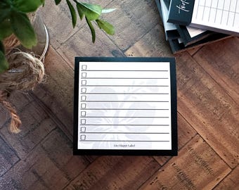 May include: A black and white notepad with a floral design at the bottom and check boxes. The notepad has the text "Live Happy Label" at the bottom. Other notepads are stacked in the background.
