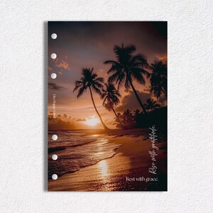 May include: A planner insert featuring a beach scene at sunset with palm trees, sand, and ocean waves. The sky is a mix of orange, yellow, and purple hues. Text on the insert reads "Rise with gratitude" and "Rest with grace."