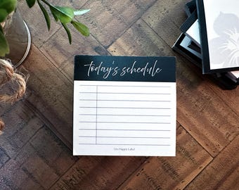 May include: A black and white notepad with the words "today's schedule" in cursive script. The notepad has lined pages for daily planning. The words "Live Happy Label" are printed at the bottom.