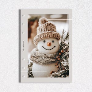 May include: A cheerful snowman wearing a knitted brown hat and scarf, with a carrot nose and a smiling face. The snowman is surrounded by evergreen branches and berries, creating a festive holiday scene.