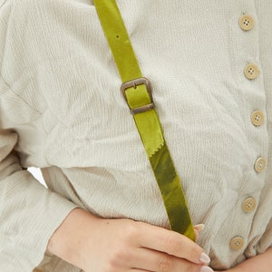 The handmade green leather bag has an adjustable strap.