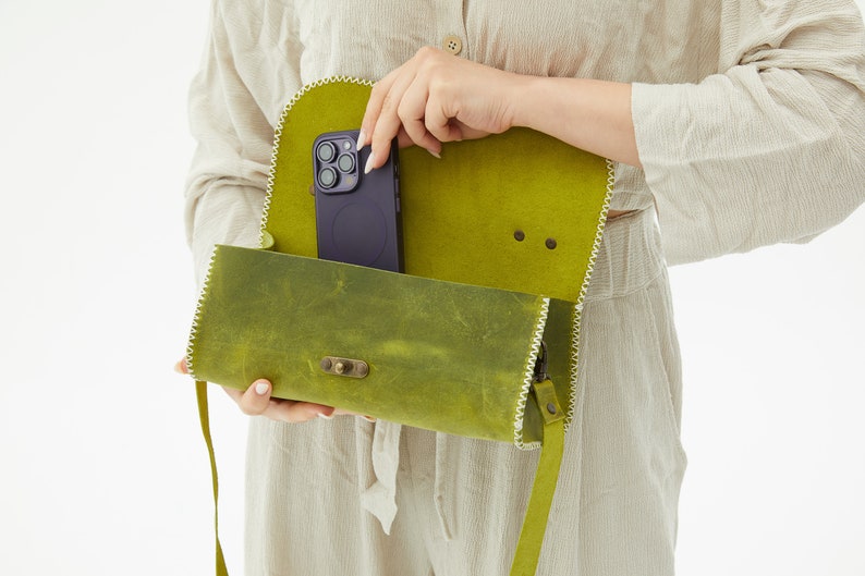 The inside of the handmade leather crossbody bag is visible. A telephone is placed inside the bag.